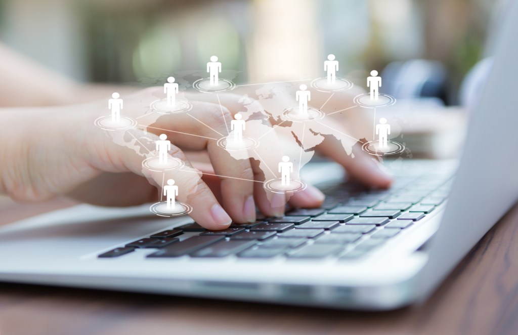 Une main tapotant sur un clavier d'ordinateur portable, avec des icônes de personnes et des connexions symbolisant le réseautage et le recrutement en ligne.
